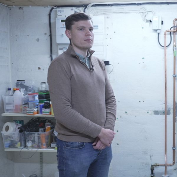 Fabian Lindh står bredvid värmepump i källare, hoppas på bidrag för energieffektivisering.