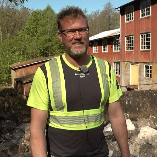Person i varselväst står framför ett rött trähus vid en byggarbetsplats eller rivningsområde.