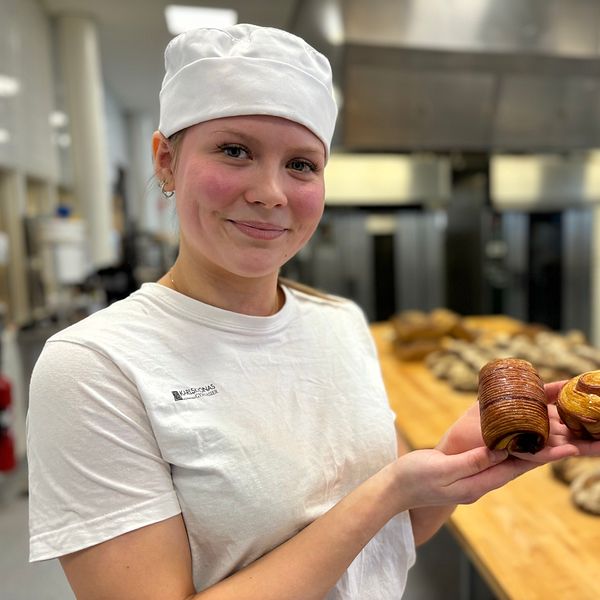 Bagare visar upp bakverk i ett bageri med bröd bakgrund.