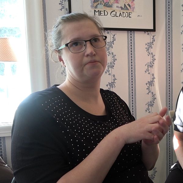 Evelina Lindberg och hennes stödperson fikar med döva kamrater i ett rum med blommiga tapeter