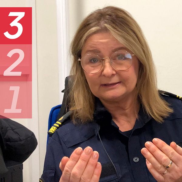 Kvinnlig polis med långt hår och glasögon sitter i förhörsrum och tittar in i kameran. Framåtlutad och gestikulerar med händerna.