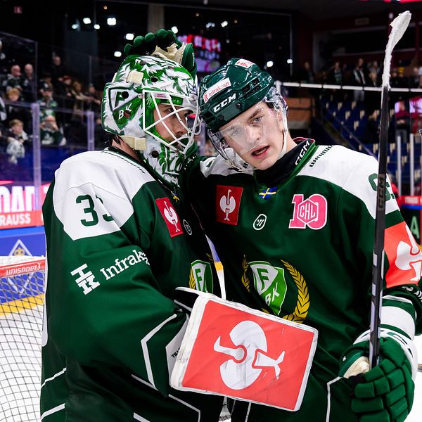 Tre hockeyspelare i gröna och vita dräkter firar en prestation på isen. De är i en jublande omfamning med hockeyutrustning på sig och en publik i bakgrunden. Det är en energisk och glad atmosfär efter en match.