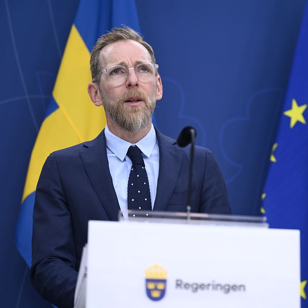 Socialminister Jakob Forssmed håller presskonferens. Bakom honom hänger svenska flaggan och EU-flaggan.