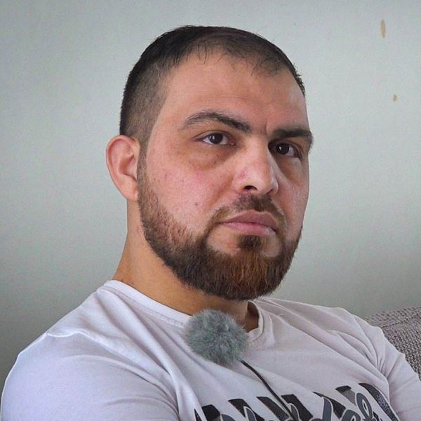 Mahmoud Alebrahim från Syrien sitter i sin soffa i sin lägenhet i Hylte och tittar in i kameran.
