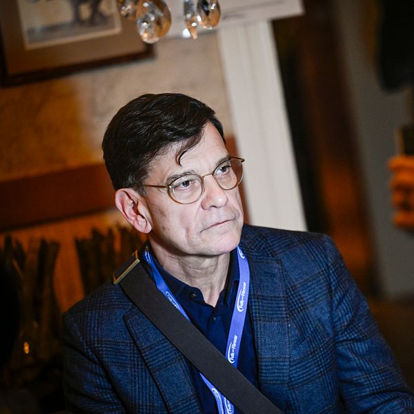Henrik Landerholm, glas lyfts i bakgrunden inomhus.