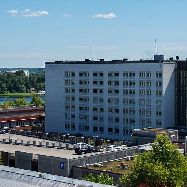 En bild med två sektioner: till vänster syns en stadsbild med ensjukhusbyggnad och parkerade bilar i förgrunden. Till höger visas porträttbild av en person som är klädd i kavaj och skjorta.