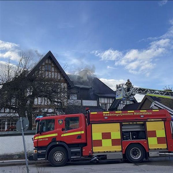 Brandbilar utanför ett rykande hus med stege mot taket.