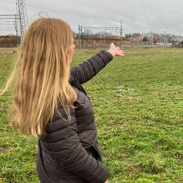 Projektledare Helena Svensson står på en äng och pekar mot en stor kulle byggt av jord