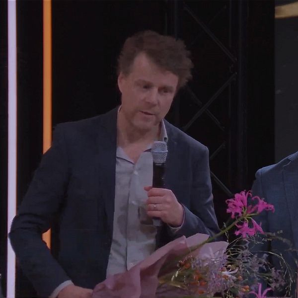 Två män står med blommor på scen