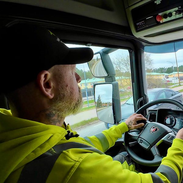 Person kör lastbil på landsväg, interiörvy av hytten.