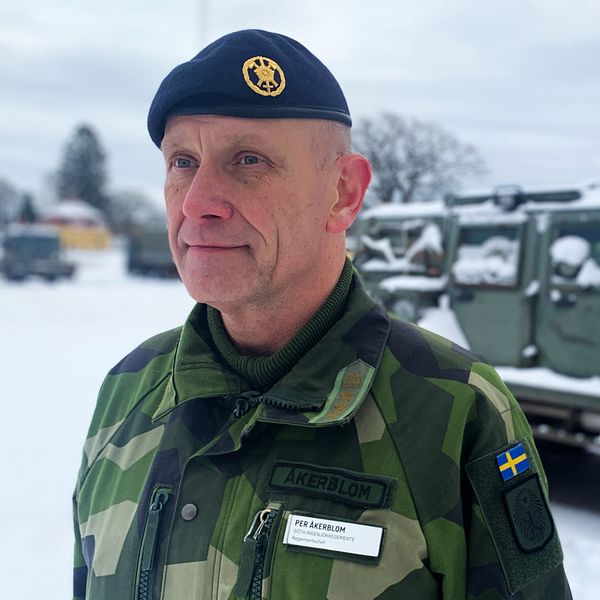 Man med blå basker och militärkläder står vid en snötäckt militärbil.