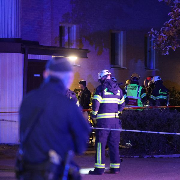 Samling av räddningspersonal och poliser arbetar vid en lägenhetsbyggnad kvällstid. En del av området är avspärrat.