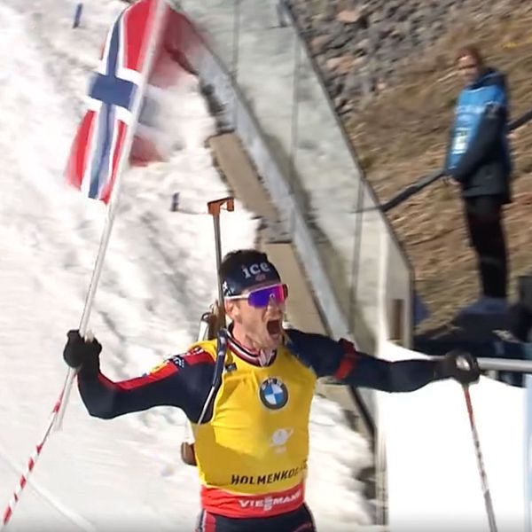 Skidåkare firar vid mållinjen med norsk flagga inför jublande publik.