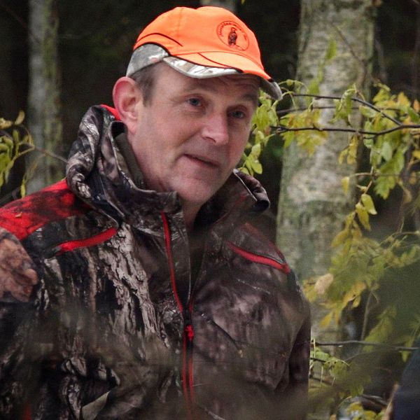Anders Olsson, ordförande i Jägareförbundet Värmland. En man i orange keps och kamouflagekläder står vänd mot kameran och tittar på reportern som står i förgrunden med ryggen mot kameran.