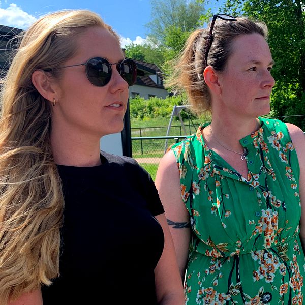 två kvinnor står utanför en skolgård. En blond kvinna i svart tröja som bär solglasögon och en kvinna med kort mörkblont hår i grön klänning