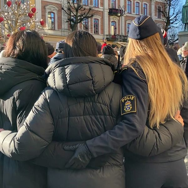 Till vänster står tre personer tillsammans med ryggen mot kameran, där en polis omfamnar två människor på ett torg omgiven av juldekorationer. Till höger visas en rad tända gravlyktor och blommor i minnesceremoni.