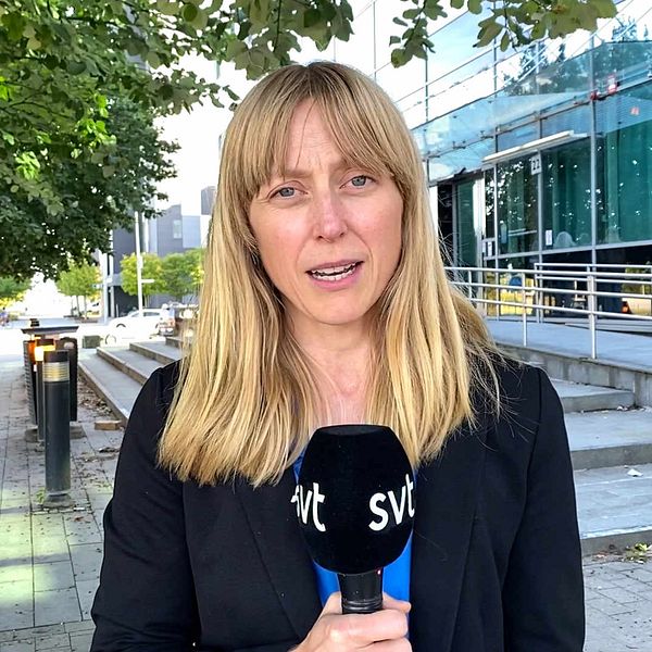 Kvinnlig reporter med mikrofon i handen. Blodstänk på marken i en busskur.
