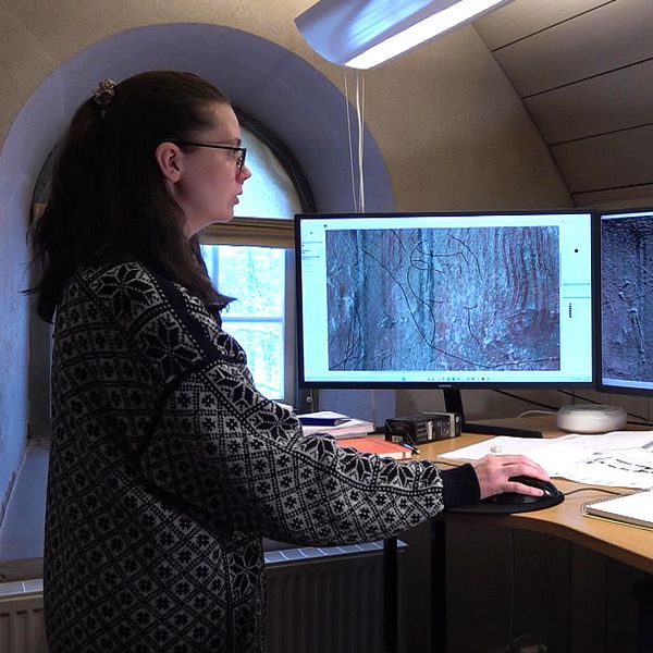 Antikvarie Annabell Fogelberg står vid sin dator på Jamtli och detaljstuderar de bilder hon tagit på gammalt klotter i Hackås kyrka