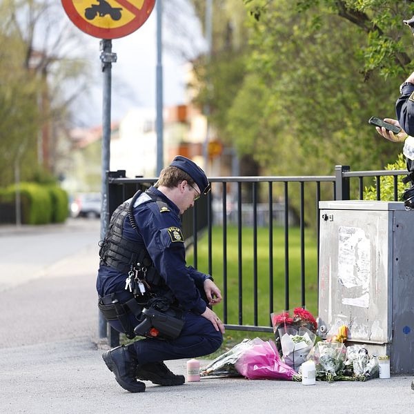 Två poliser vid en minnesplats med blommor på en trottoar.