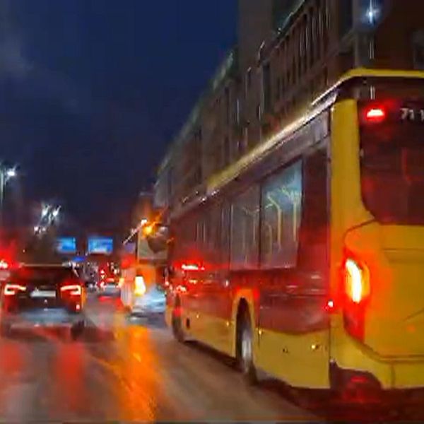 Gult bussfordon som körs längs en stadsgata i mörker, med röd belysning bak och en skylt som visar linje 4. Andra bilar är synliga i närheten, och gatan reflekterar ljuset från bilarna.