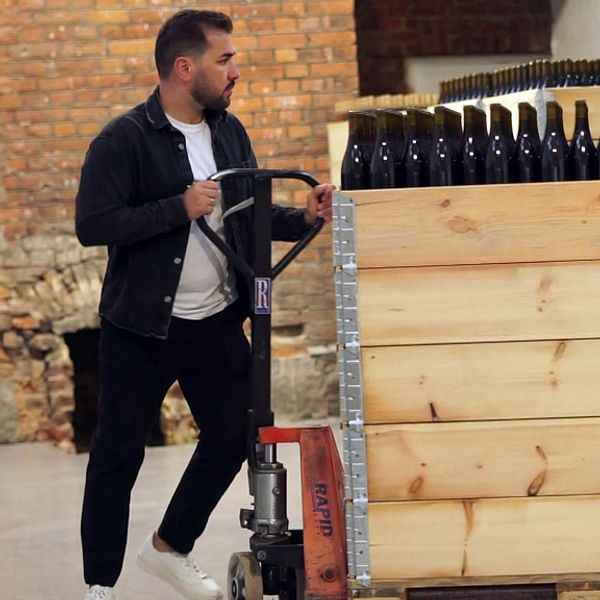 En man som kör en stor pall lastad med vinflaskor.