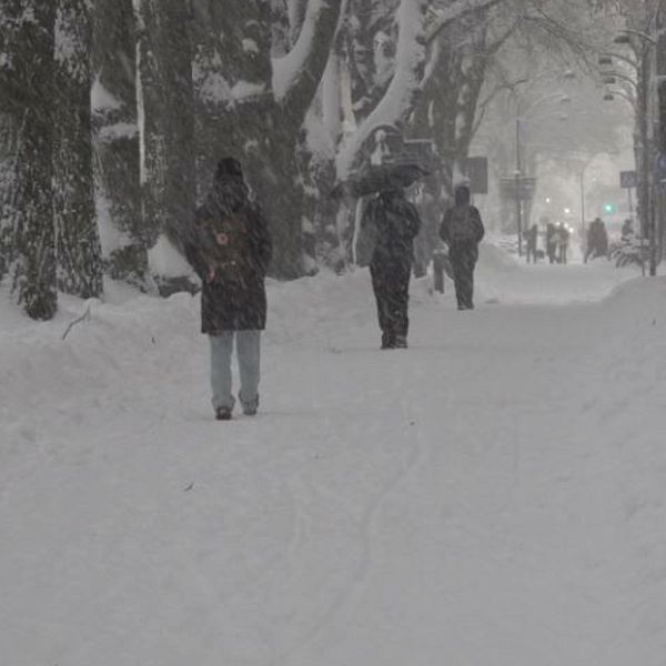 Bild på en gata med snö och en kvinna utomhus.