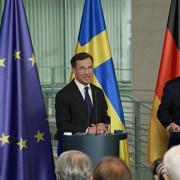 Presskonferens med två talare vid podium, där den svenska flaggan och den tyska flaggan är synliga. Bakom dem står EU-flaggor, vilket understryker det europeiska samarbetet.