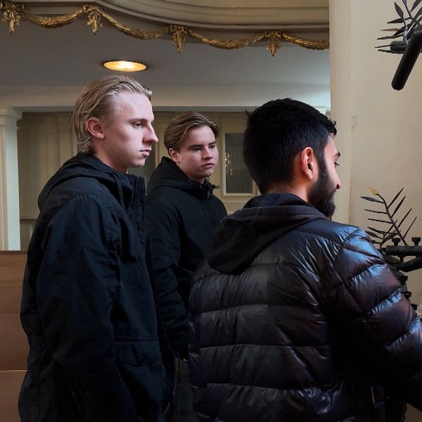 Tre personer, två med ljust hår och en med mörkt hår, står i en kyrka vid ett ljusträd och tänder ljus.