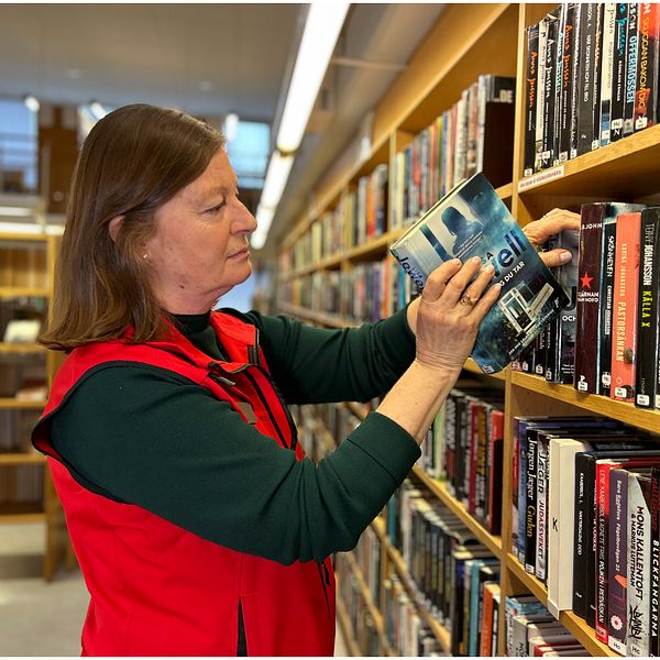 En bibliotekarie som lägger in en bok i hyllan till vänster i bild. En väktare till höger i bild.