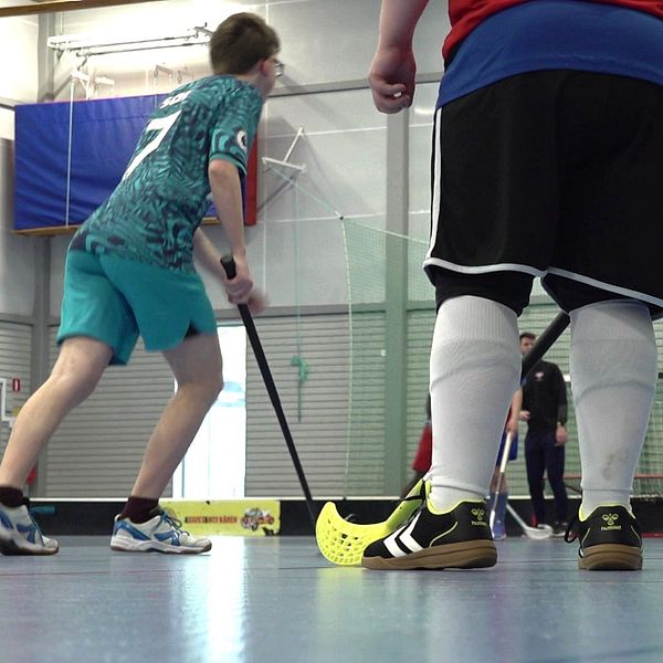 Unga spelare spelar innebandy i en idrottshall. Klubbfäktning nära målet.