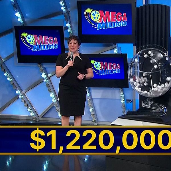 En programvärd står framför två lotterikuponger och en stor skärm med texten ”Mega Millions”. En stor summa, $1,220,000,000, visas tydligt i bildens nedre del, vilket indikerar det aktuella jackpotbeloppet.