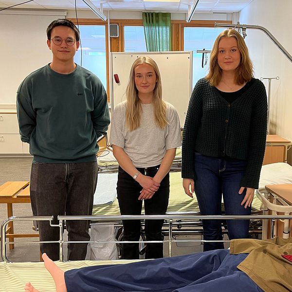 Tre elever framför en säng där det ligger en docka