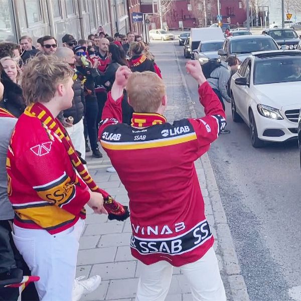 Supporters samlas på trottoaren bredvid stillastående bilar och en polisbil.
