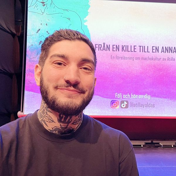 En person, Atilla Yoldas,  sitter framför en stor scen med en presentation som visar titeln ”FRÅN EN KILLE TILL EN ANNAN” och texten ”En föreläsning om människo­kultur av Atilla Yoldas”. Bakgrunden är färgglad med illustrationer och information om att följa föreläsningen på sociala medier.