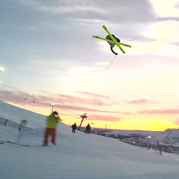 Vy över skidbacken i Kiruna där en utförsåkare gör ett trick högt upp i luften med skidorna korsade samtidigt som hen roterar i luften.
