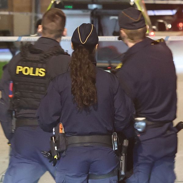 Fyra poliser står vid avspärrning, polisfordon med blåljus syns i bakgrunden.