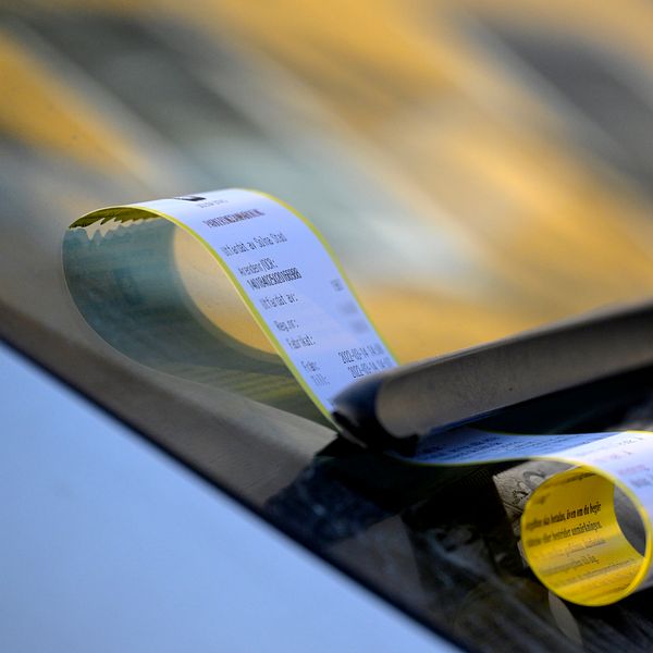 Parkeringsbot fäst på vindrutetorkaren av en bil, med rullen av betalningskvitton delvis synlig.