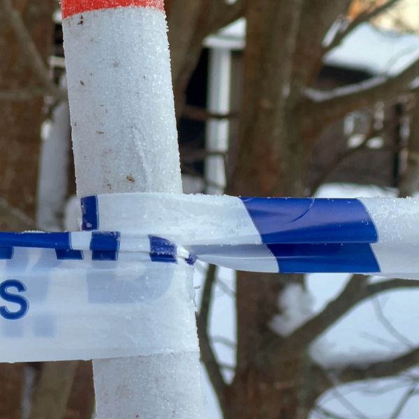 Polisavspärrning med rimfrost omger ett område bland vinterträden. I bakgrunden syns ett hus.