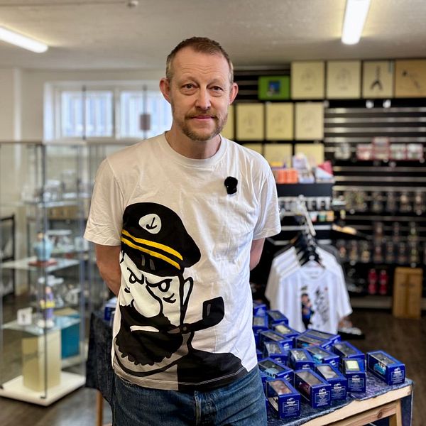 Person med vit t-shirt står i butik med hyllor fyllda av olika varor och tryckta t-shirts.