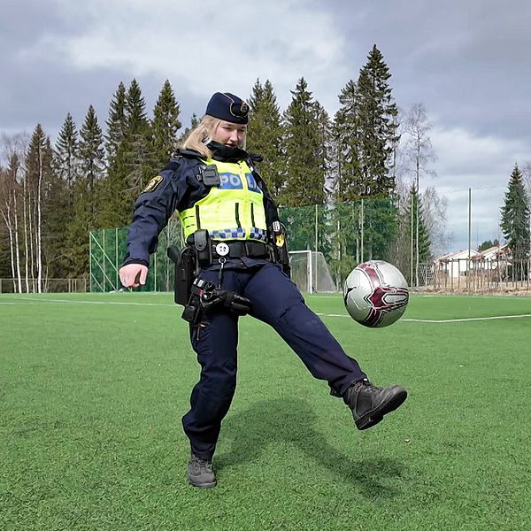 En polis jonglerar med en fotboll på en gräsplan utomhus framför träd och skog.