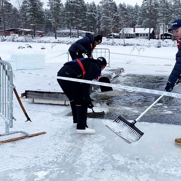 tre personer skottar upp is vid en frusen sjö