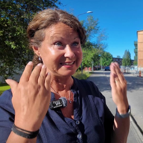 Person gestikulerar på gata med nybyggda bostadshus i bakgrunden en solig dag.