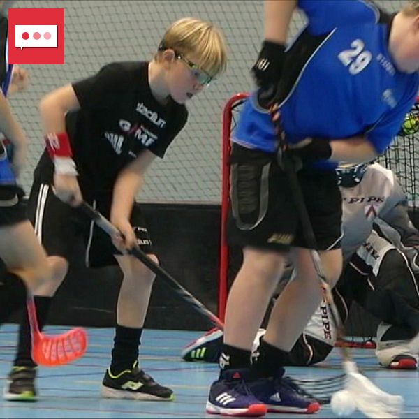 Tre unga spelare spelar innebandy på en sporthall, med en målvakt i bakgrunden.