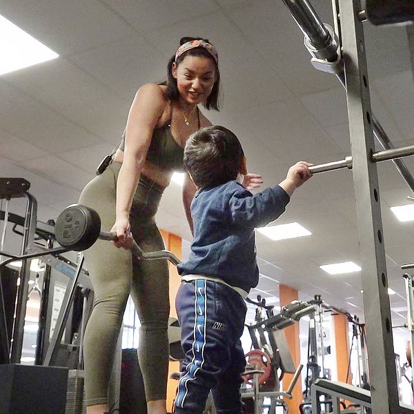 Mamma tittar på sitt barn på gymmet och håller en vikt, ser glad ut