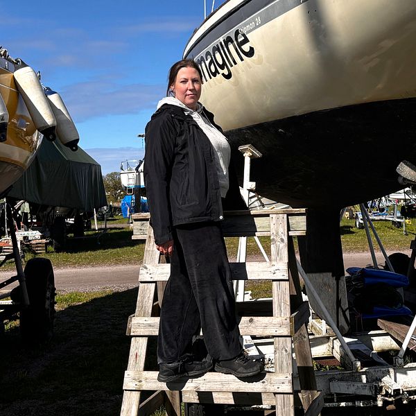 En person står på stege vid en uppställd segelbåt på en uppläggningsplats.