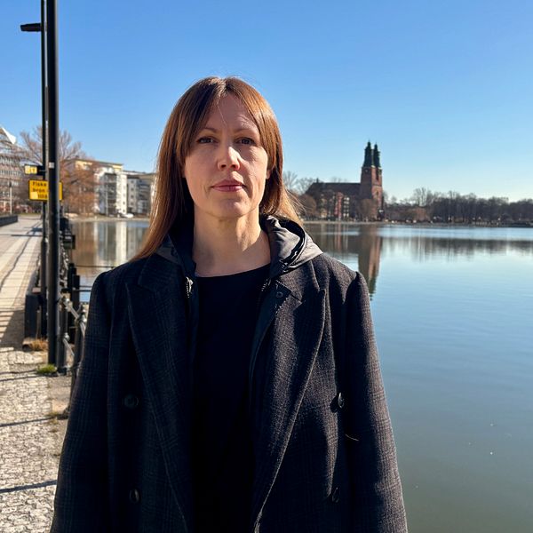 Person vid sjöpromenad under klarblå himmel. Stadssilhuett och kyrka i bakgrunden.