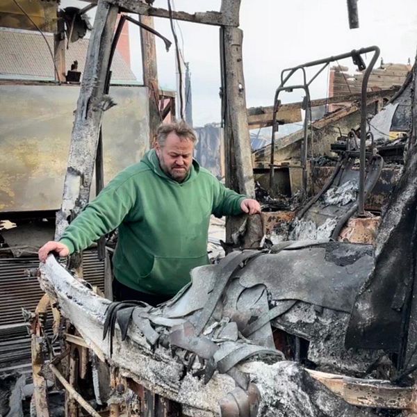 Man inspekterar en utbränd buss, rester och skadade säten synliga.