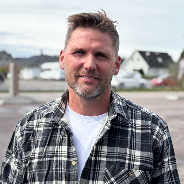 Person i rutig skjorta står på en tom parkering med hus i bakgrunden.