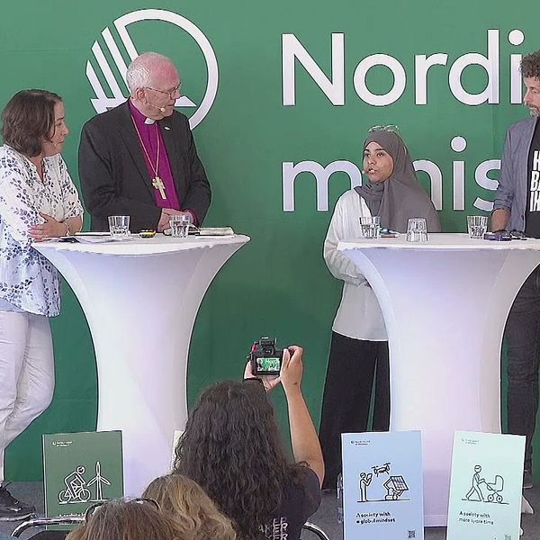 En panel med fyra personer + moderator vid ståbord på en scen i Almedalen diskuterar grön omställning och om det kan vara vägen till ett lyckligare liv.