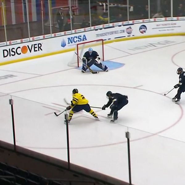 Ishockeyspelare i gul tröja skjuter mot mål, försvarare och målvakt försöker stoppa pucken.